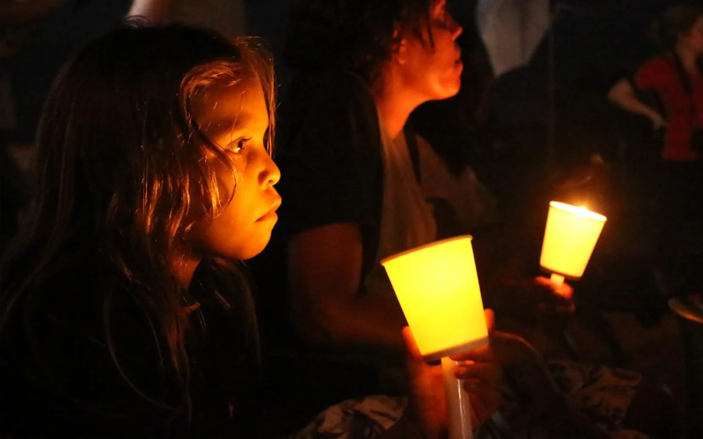 An Aboriginal girl holds a lantern in the dark, another girl sits beside her