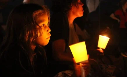 An Aboriginal girl holds a lantern in the dark, another girl sits beside her