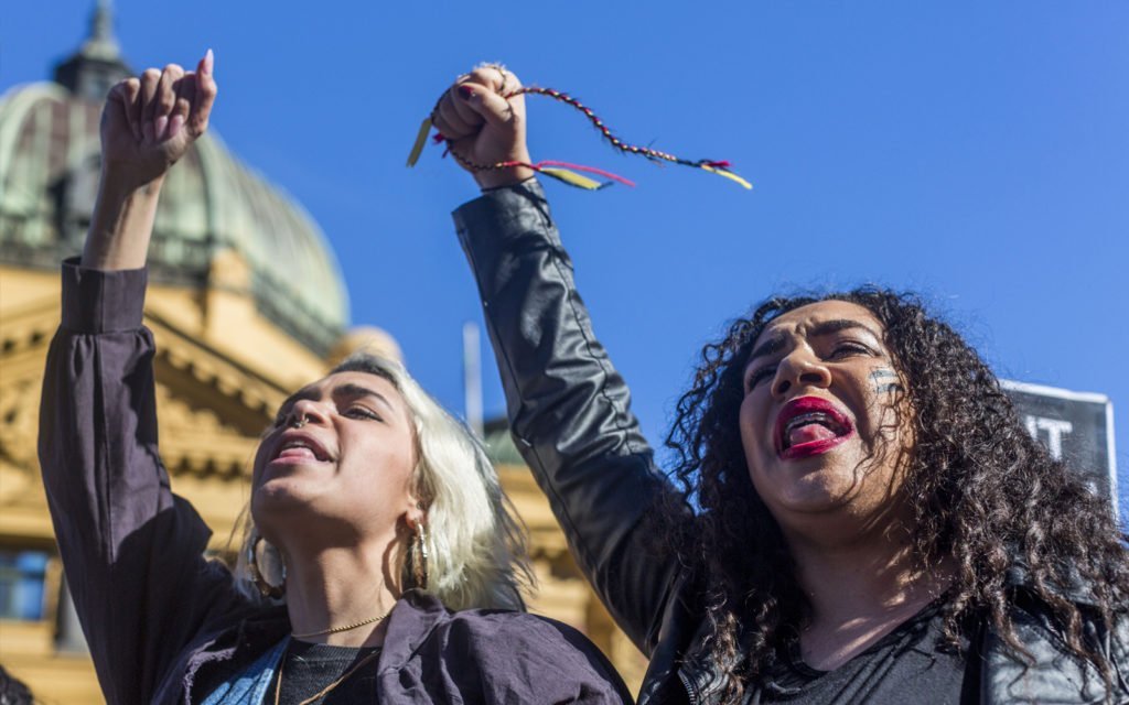 Two women with their fists in the air holding yellow, red and black ribbons.