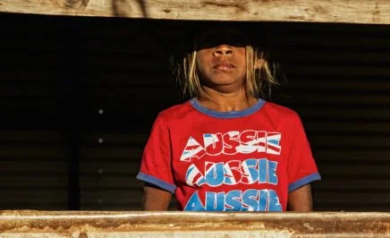 Aboriginal girl looking through old window, wearing a red t-shirt with 'Aussie' on it. Broome, Western Australia.