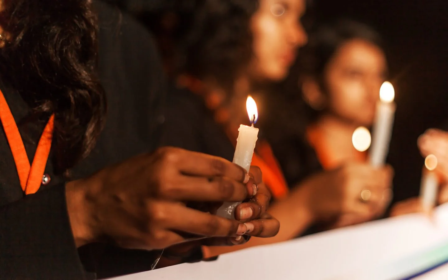 people marching behind a banner, holding candles. Shot is a close up of a hand holding candle.