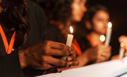 people marching behind a banner, holding candles. Shot is a close up of a hand holding candle.