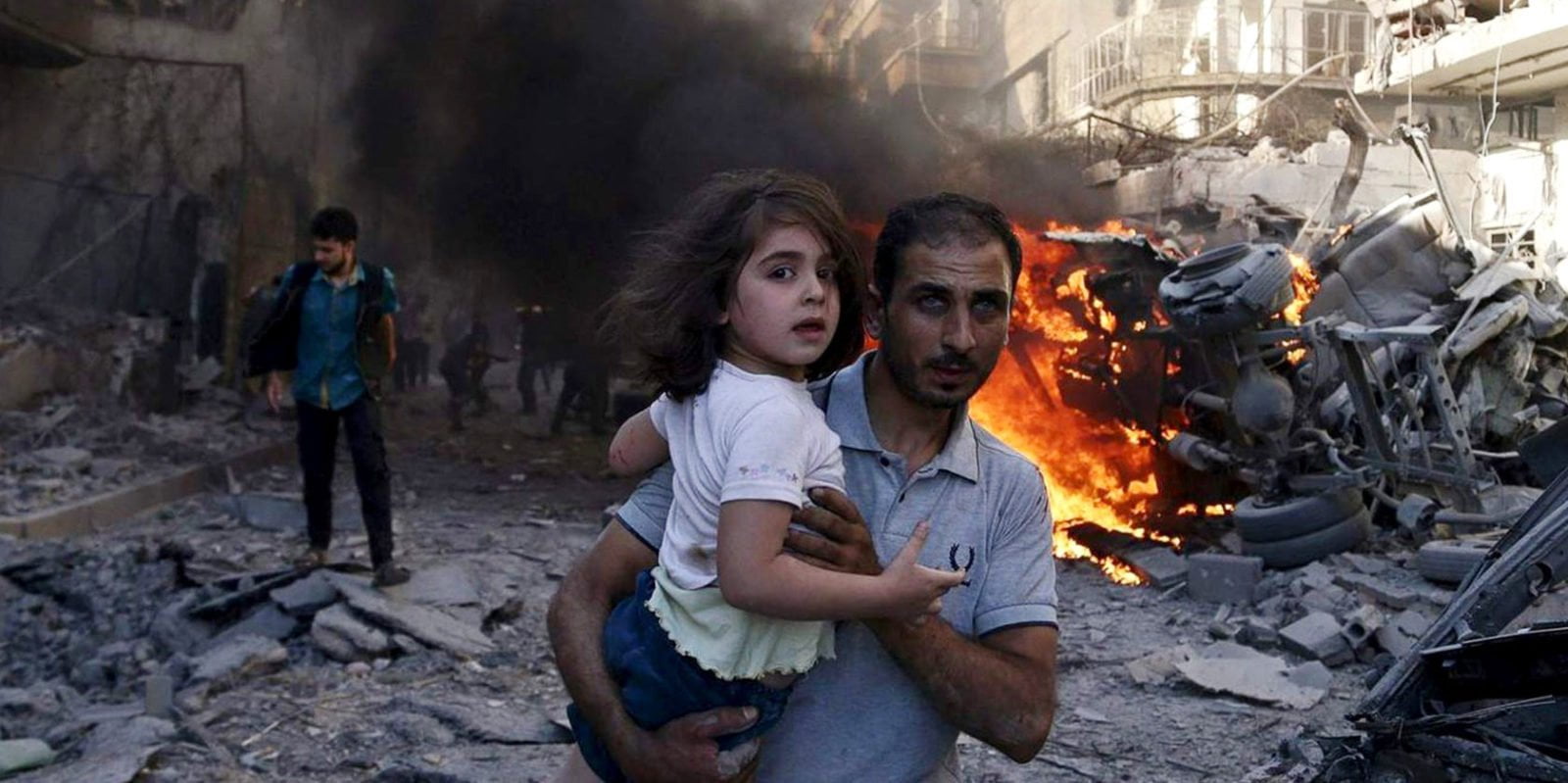 A man carries a young girl through rubble in Syria.