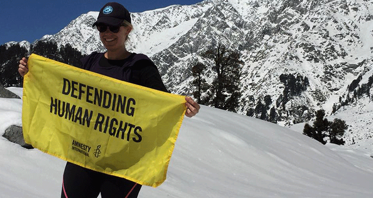 Amanda holding a yello amnesty banner stating 'defending human rights' in the snow in front of a mountain