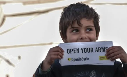 A young boy holding a Open to Syria campaign sign