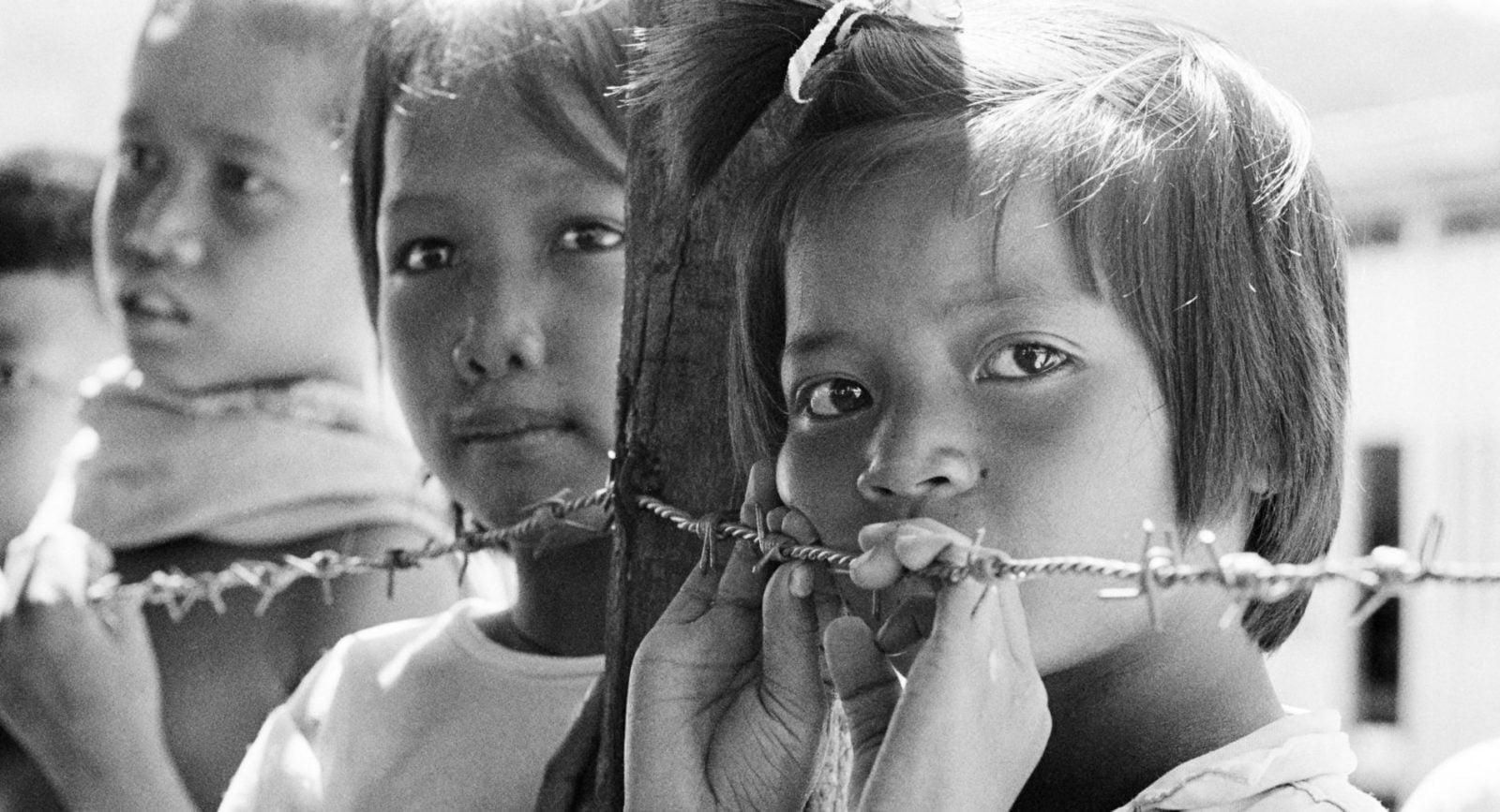 Three young refugees children leaning against barbed wire in South East Asia