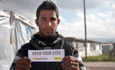 A Syrian refugee in Lebanon holding a sign that reads 