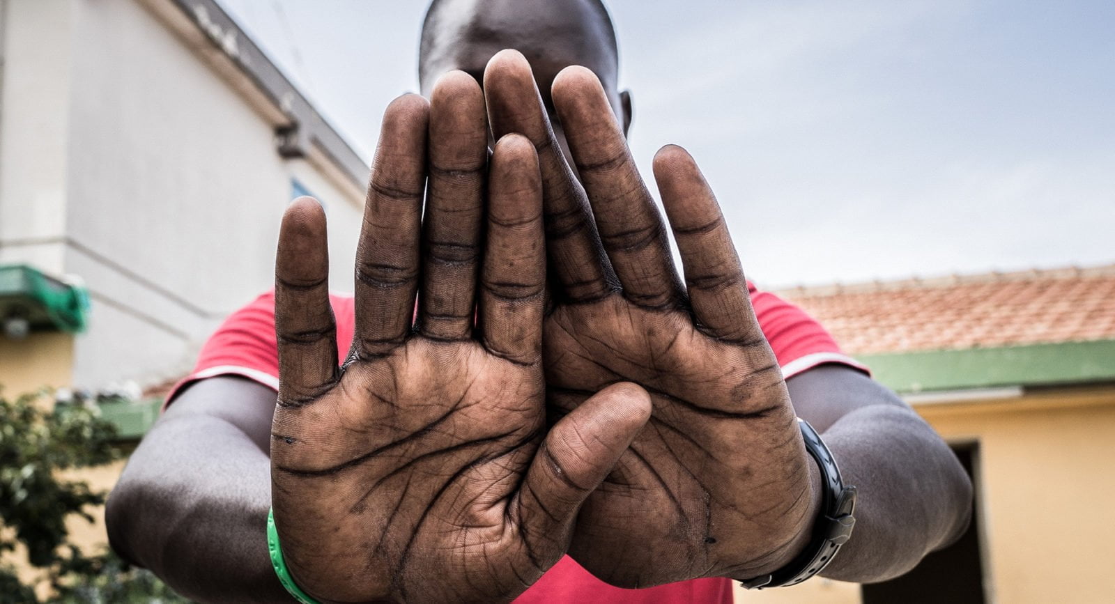 A young man from Gambia holds his hands in front of the camera, covering his face