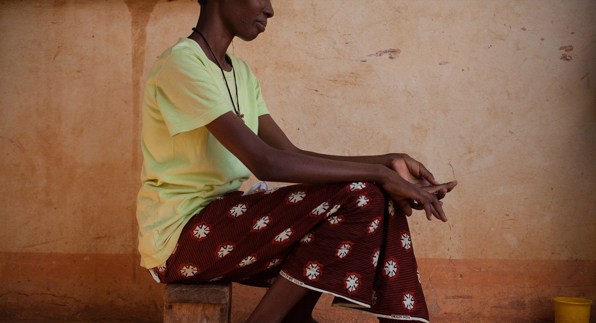 A woman seated on a wooden bens with a red skir and her hands in her lap