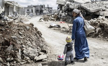 A Kurdish Syrian woman walks with her child past the ruins of the town of Kobane