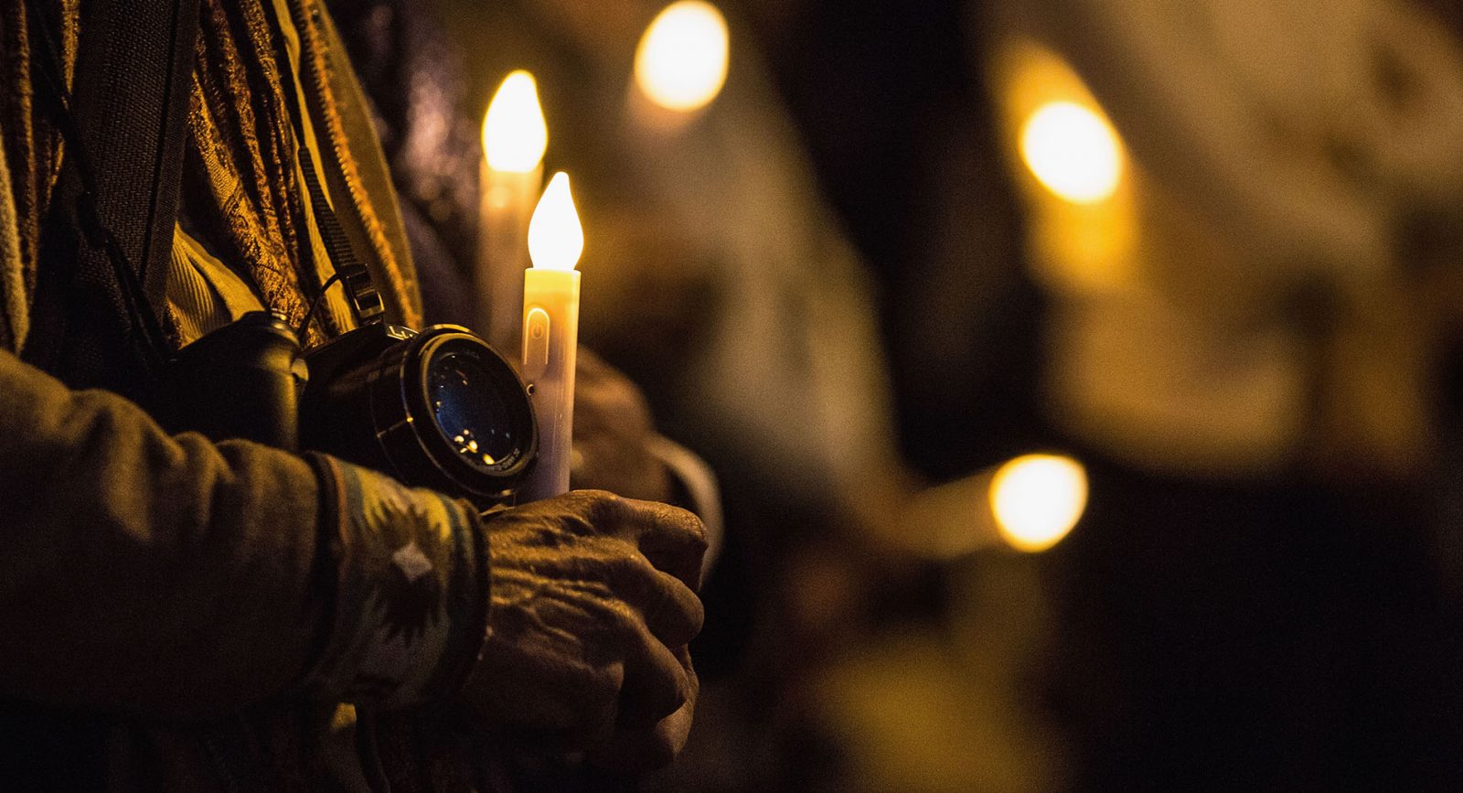 An activist holds a camera and a candle at a vigil