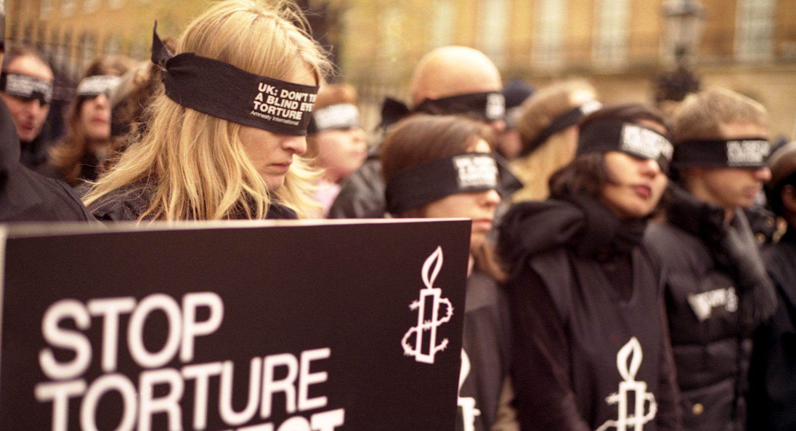 Activists at UK rally wearing 'Stope torture' shirts and blindfolds over their eyes.