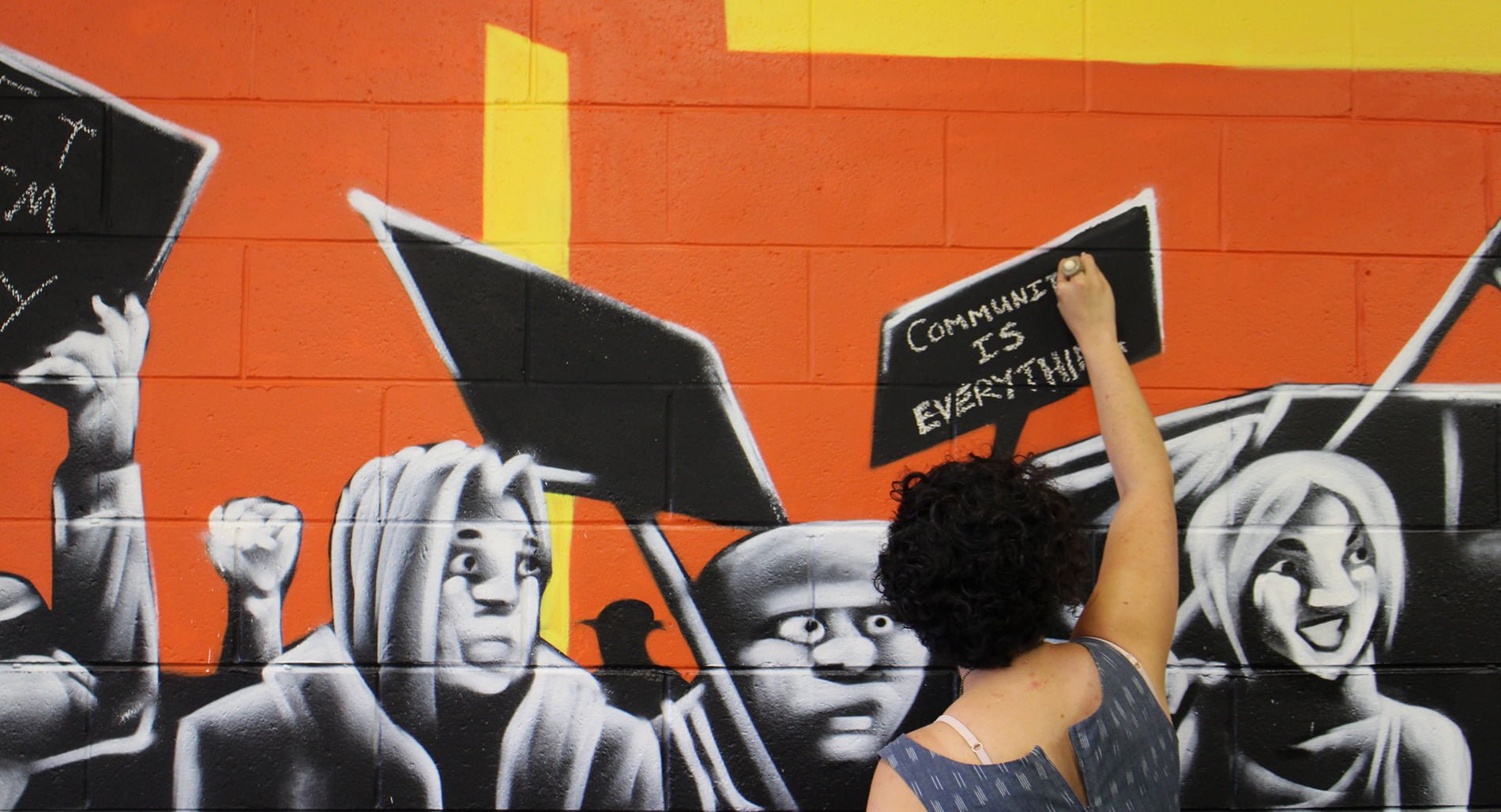 Activist Camille Furtado writing "Community is Everything" on Brisbane action centre art wall