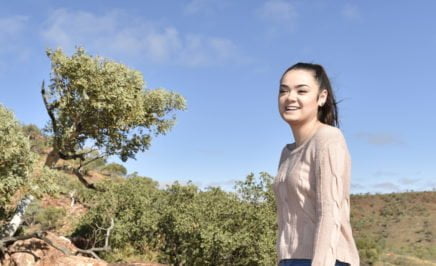 Young woman Justice King stands on a hilltop and laughs, with a rolling countryside view around her.