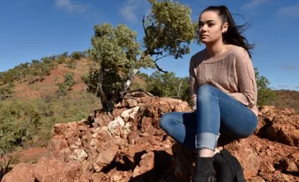 Justice King, a young Indigenous advocate, sits on an escarpment of orange rock
