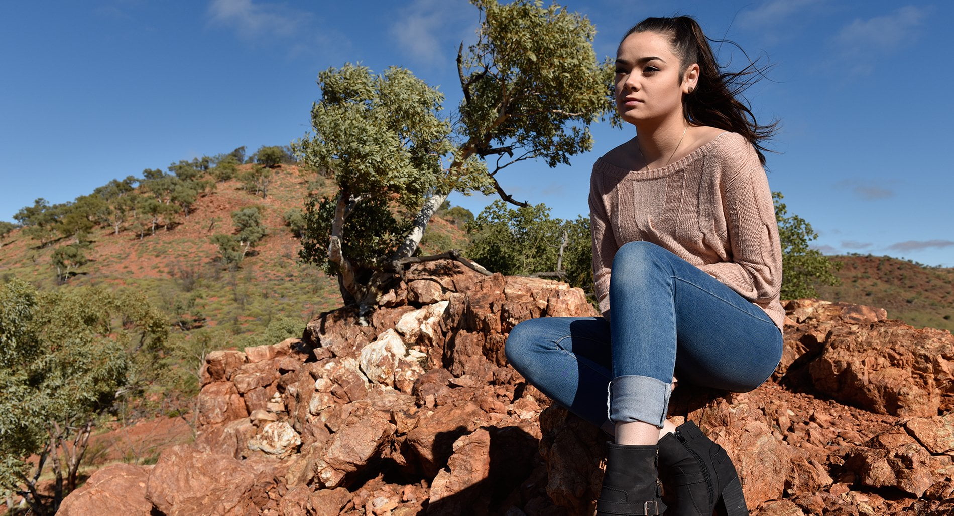 Justice King, a young Indigenous advocate, sits on an escarpment of orange rock