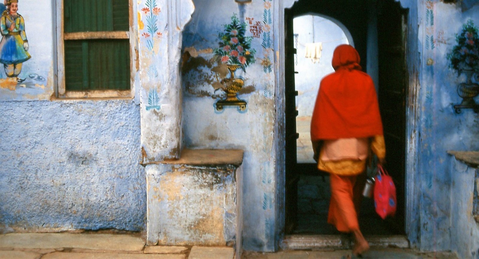 A person dressed in red walking through a blue doorway in India