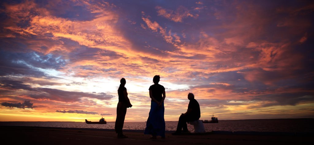 Three Indigenous people silhouetted at sunset by the ocean