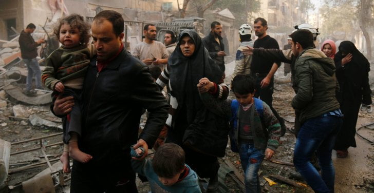 A line of men, women and children walk in a line through rubble
