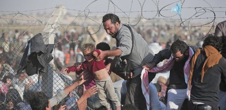 A man in a crowd lifts a child over a fence