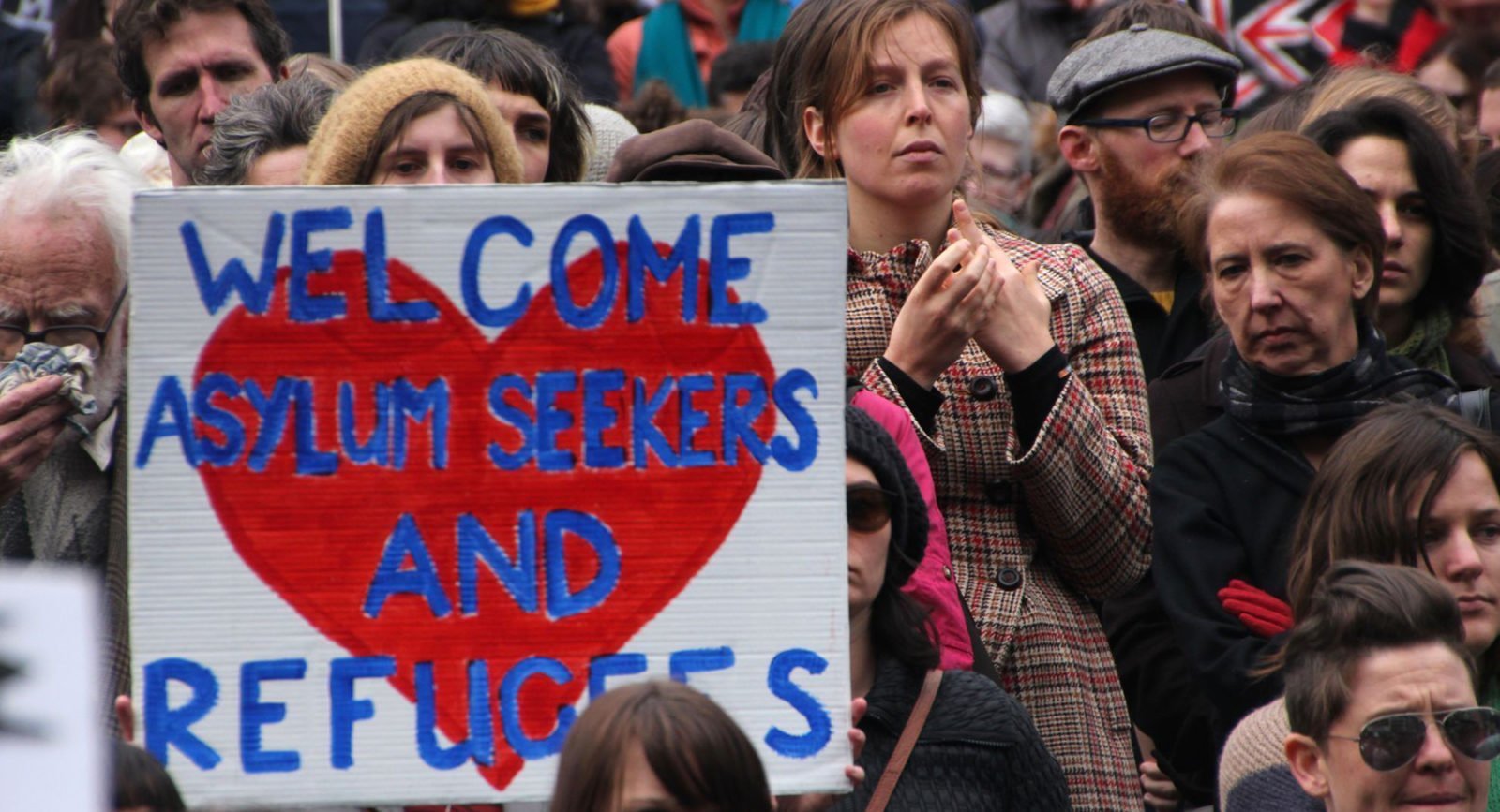 A protester holds a sign reading 'Welcome asylum seekers and refugees'