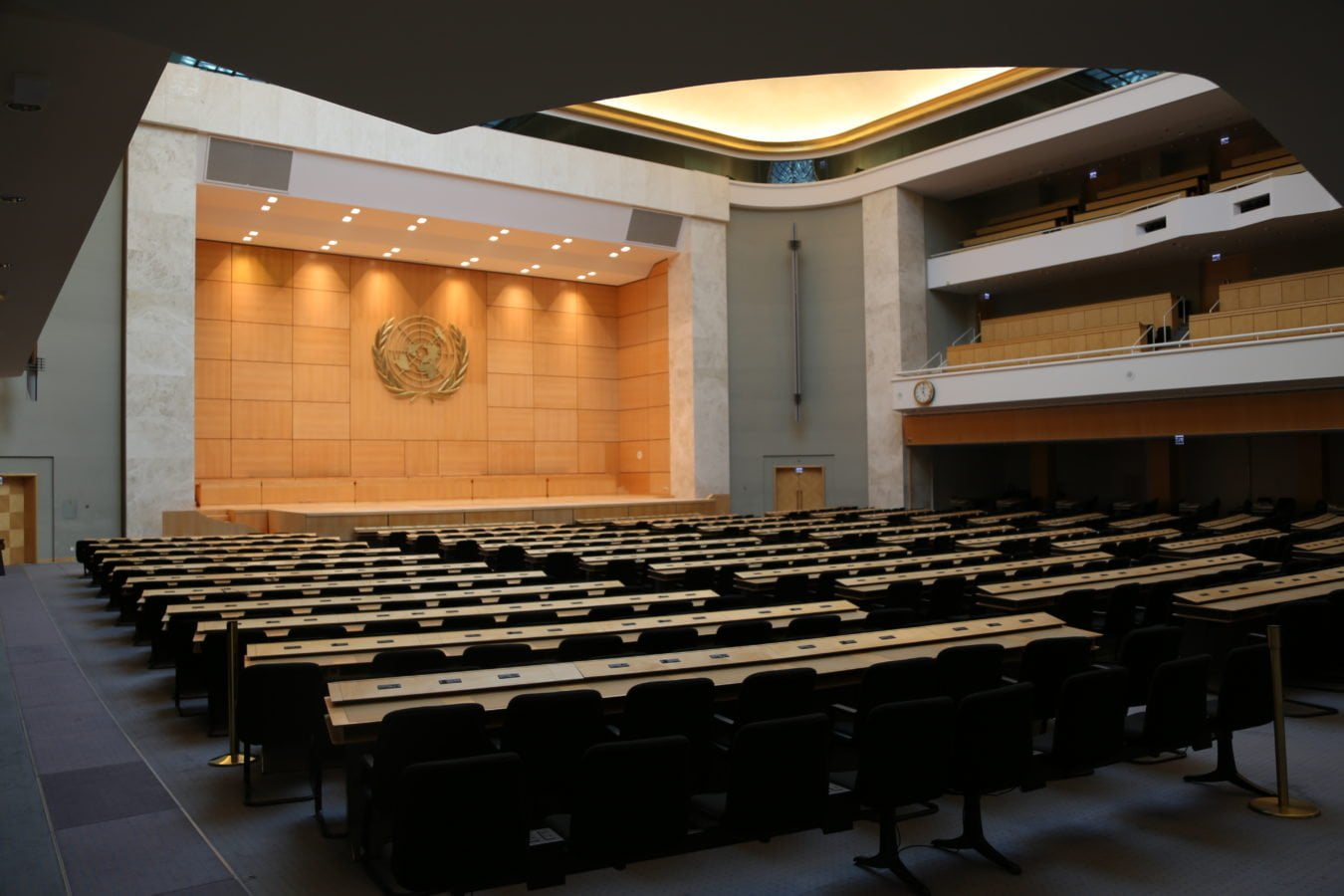 Interior photograph of the large international meeting chamber room at the UN in Geneva, Switzerland. The room is empty.