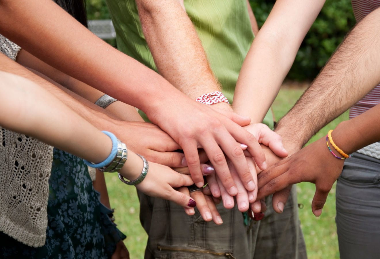 The arms of several people are stacked in the center of the image. &copy; iStock/cate_89