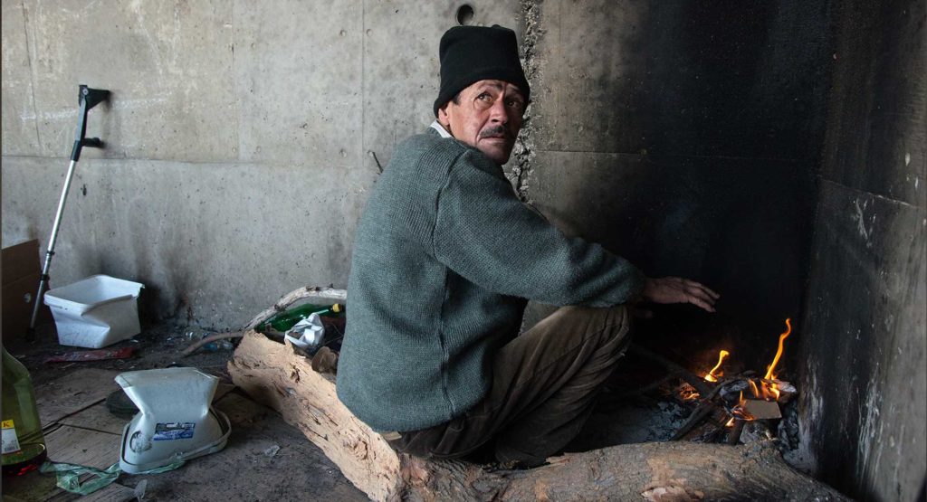 A refugee sits in front of a fire in an abandoned building