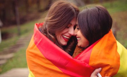 Two women embracing inside a rainbow flag
