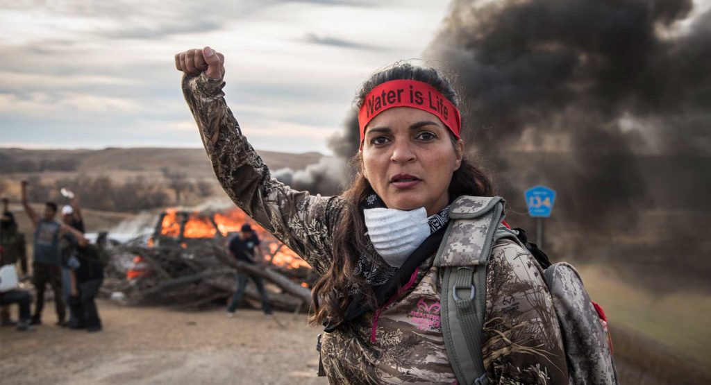 A Field Medic wearing camo and a red headband that reads: "Water is Life"