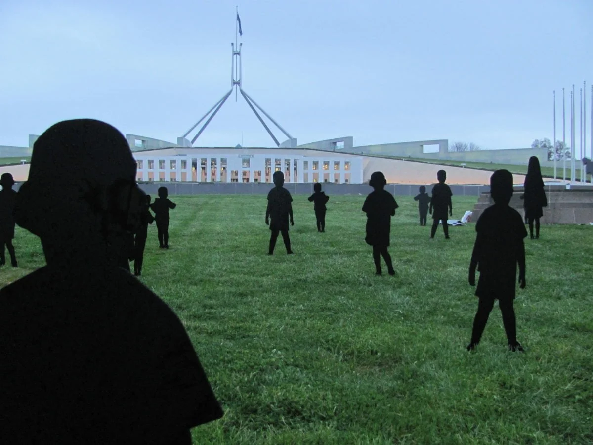 Cardboard silhouettes of children on the lawn outside parliament house