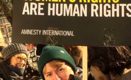 A woman in a beanie holds a sign that says 'Women's rights are human rights'