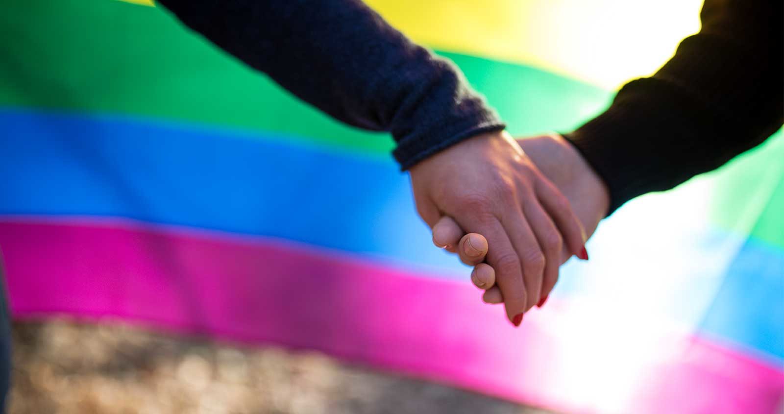 Two people holding hands in font of a rainbow flag