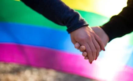 Two people holding hands in font of a rainbow flag
