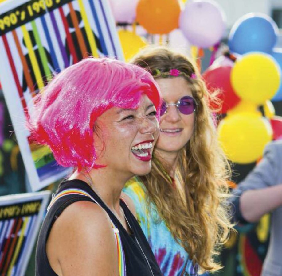 A young woman wearing a pink wig with colourful balloons in the background