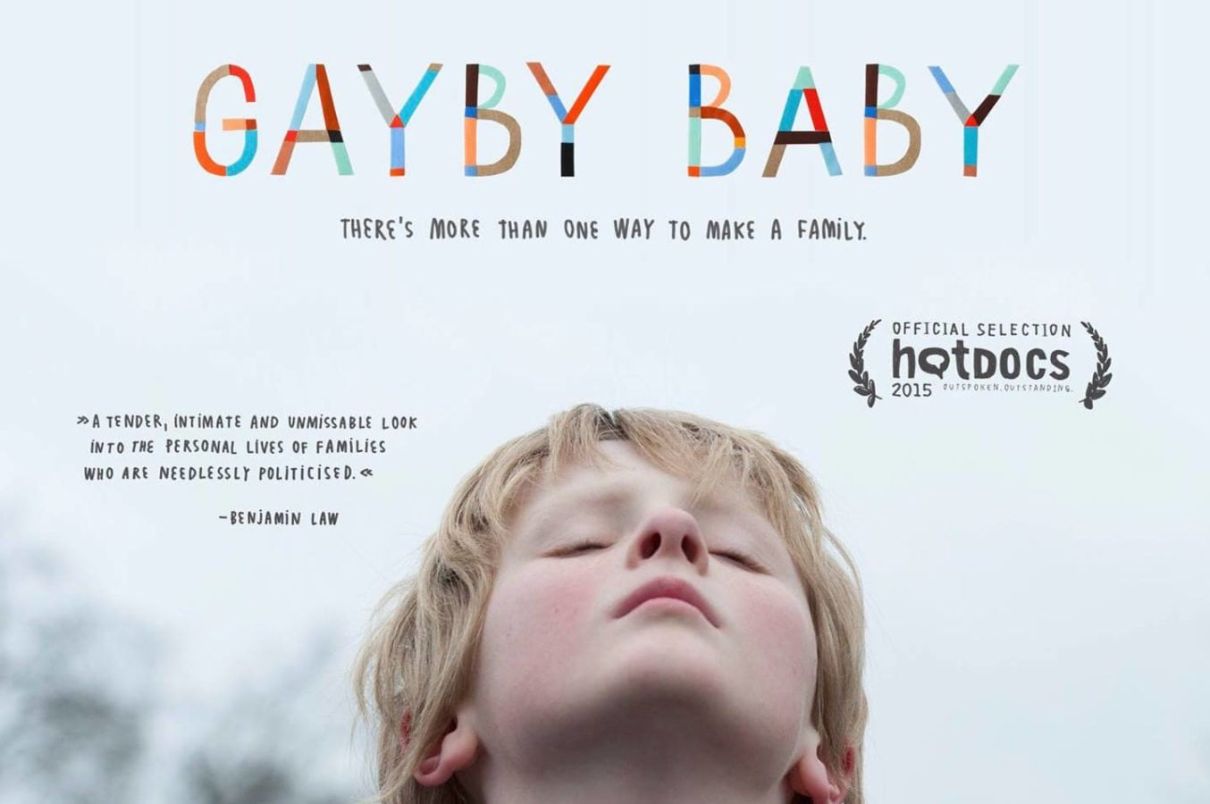 Gayby Baby Film Poster - image of a blonde boy with a light blue sky in the background, with rainbow lettering spelling out 'Gayby Baby'