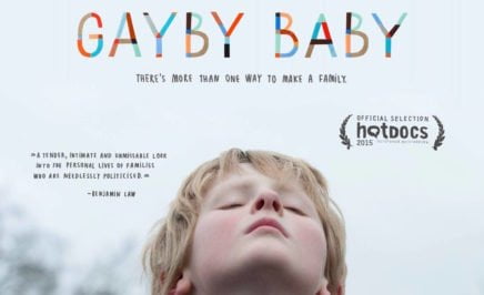 Gayby Baby Film Poster - image of a blonde boy with a light blue sky in the background, with rainbow lettering spelling out 'Gayby Baby'