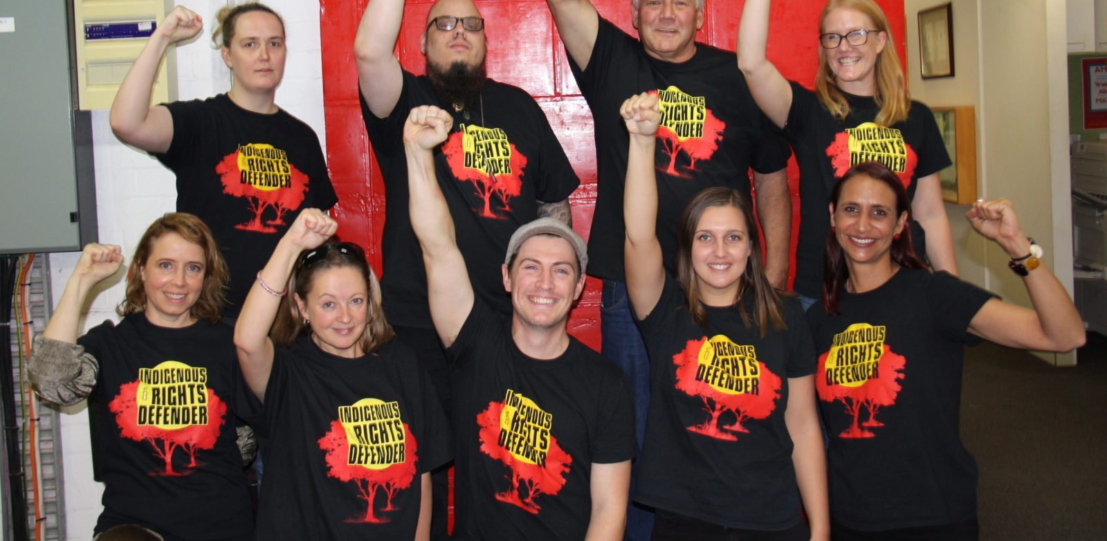 9 people with their fists held high with Indigenous Rights Defender on their t-shirts