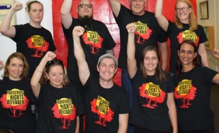 9 people with their fists held high with Indigenous Rights Defender on their t-shirts