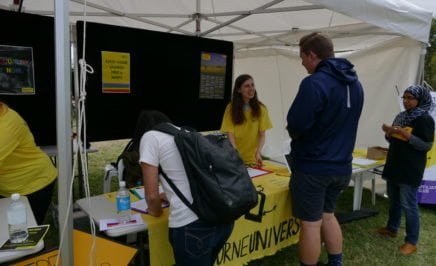 A volunteer stands behind a table, with a yellow banner that reads 