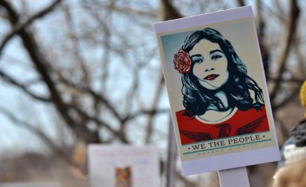 A protester holds up a poster of a woman with a rose behind her ear, as designed by artist Shepard Fairey.