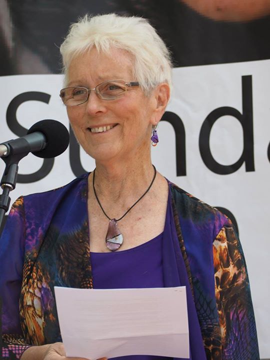 Sister Jane Keogh, an elderly woman, holds a piece of paper and speaks into a microphone