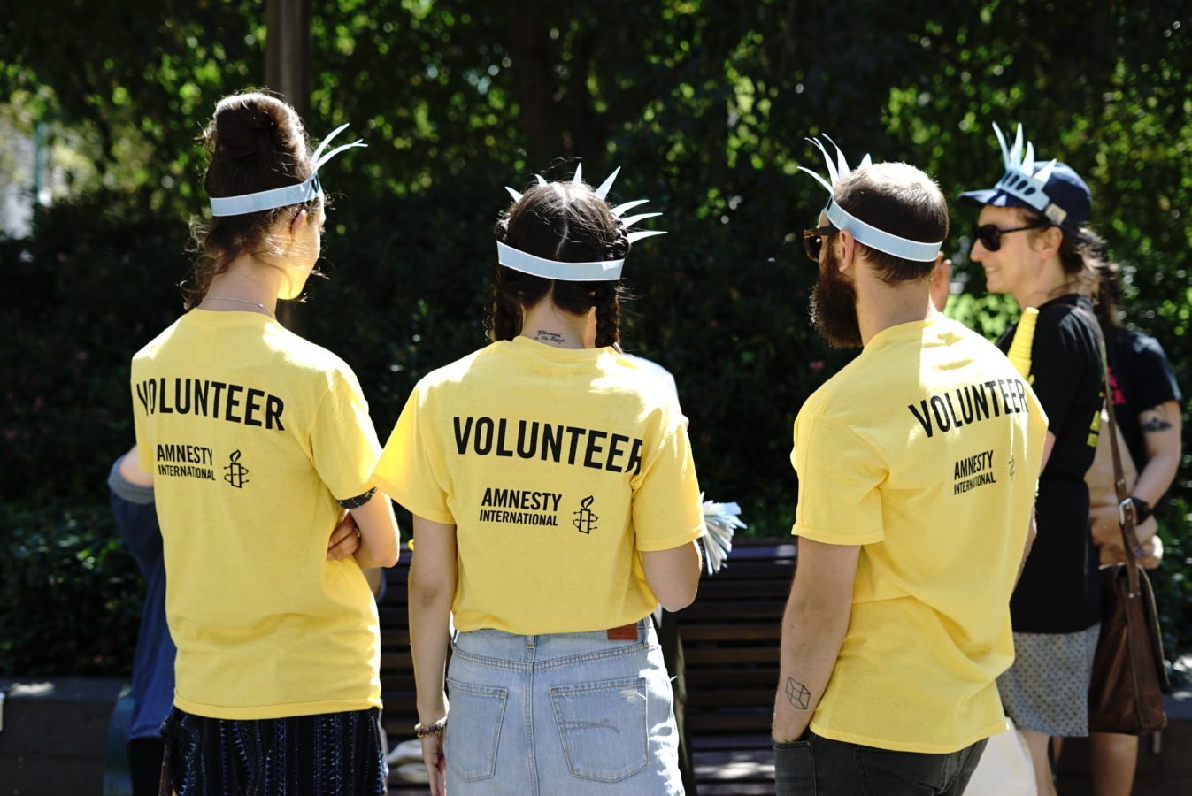 3 people with their backs to the camera show yellow volunteer t shirts
