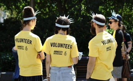 3 people with their backs to the camera show yellow volunteer t shirts