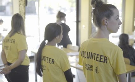 3 volunteers stand wearing yellow 'volunteer' shirts