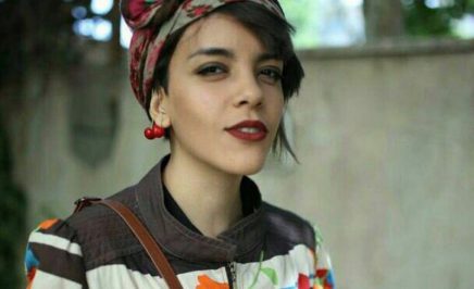 Iranian women's rights defender, Yasaman Aryani wearing a colourful head scarf and jacket in front of a grey wall.