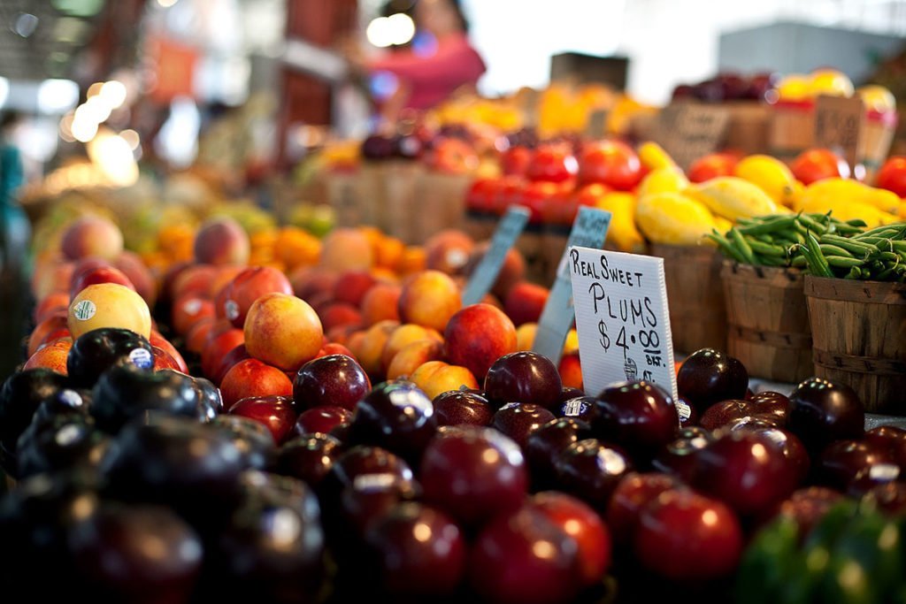 A close up shot of a fruit stall at a farmer's market in Dallas. The produce featured includes plums, apples, and lemons.