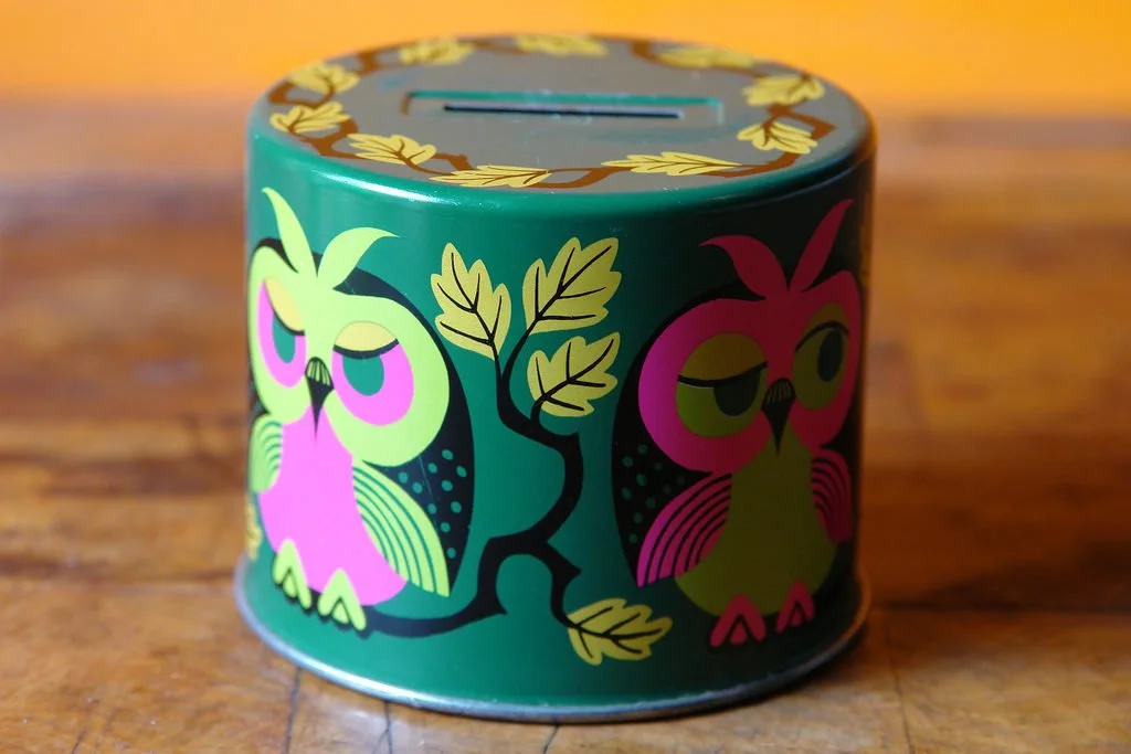 A round money box painted green, with painted florals and owls on it.