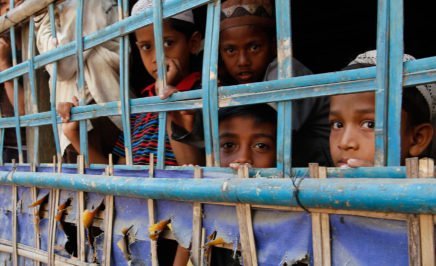 Rohingya children peer out from behind a fence in a rural village in Myanmar.
