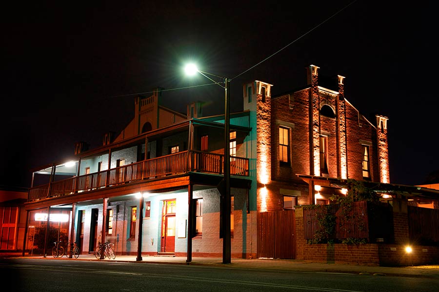 Photograph of the outsdie of a hotel with a balcony at night